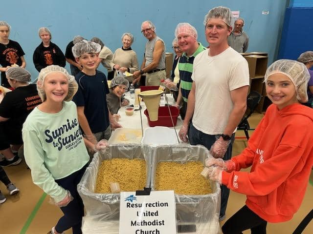 Youth packing meals alongside adults